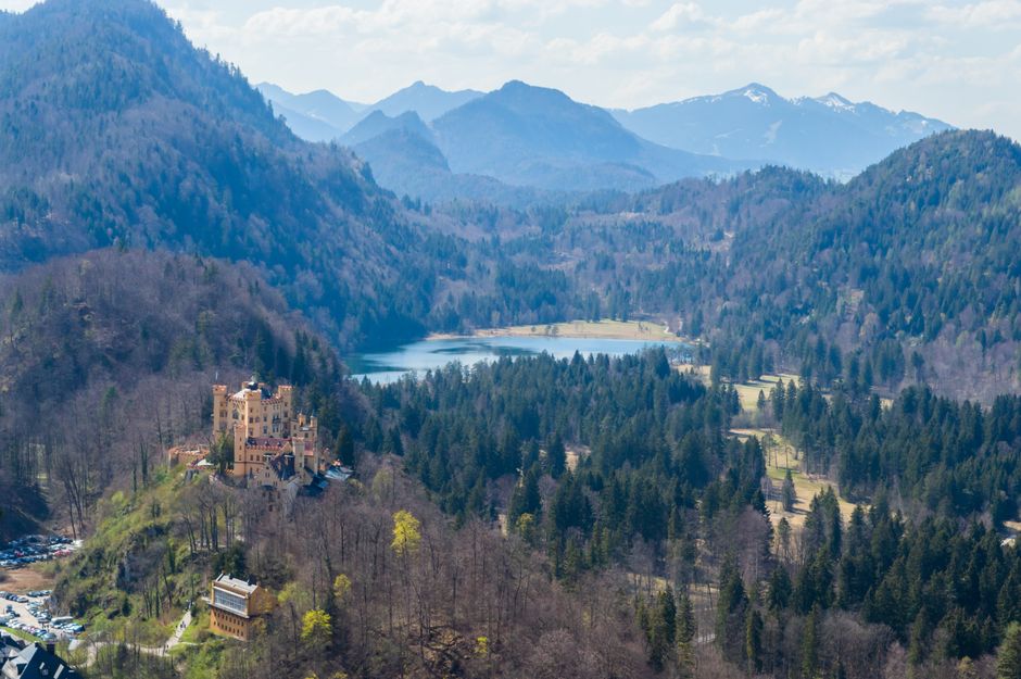 Stunning aerial view of Hohenschwangau Castle in Bavaria, framed by lush forests and mountains.